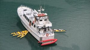 Aerial view of Alaska ship Snow Goose sitting in calm water on a rainy day, with a group of yellow kayaks tied onto each side.