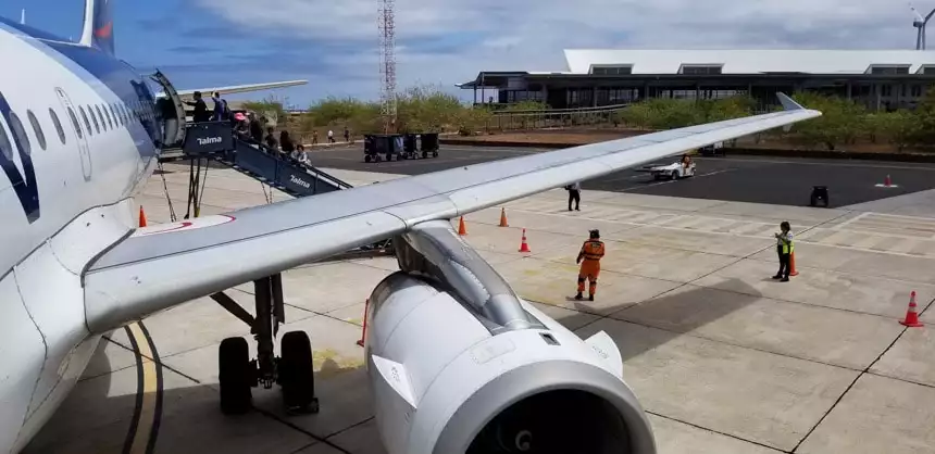 The tin-roofed Baltra Galapagos airport seen from an airplane stairway with the engine and wing in the foreground 