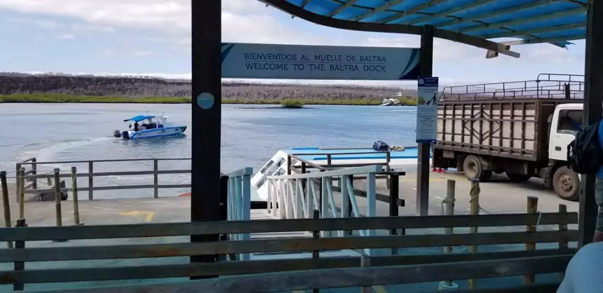 Sign that says Welcome to the Baltra Dock with a small boat sailing behind it.