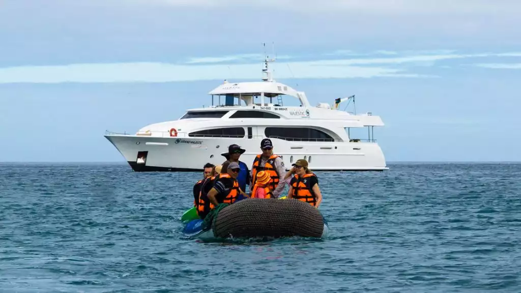 Panga boat with Grand Majestic Galapagos travelers in life jackets motors away from the ship on a sunny day with calm seas.