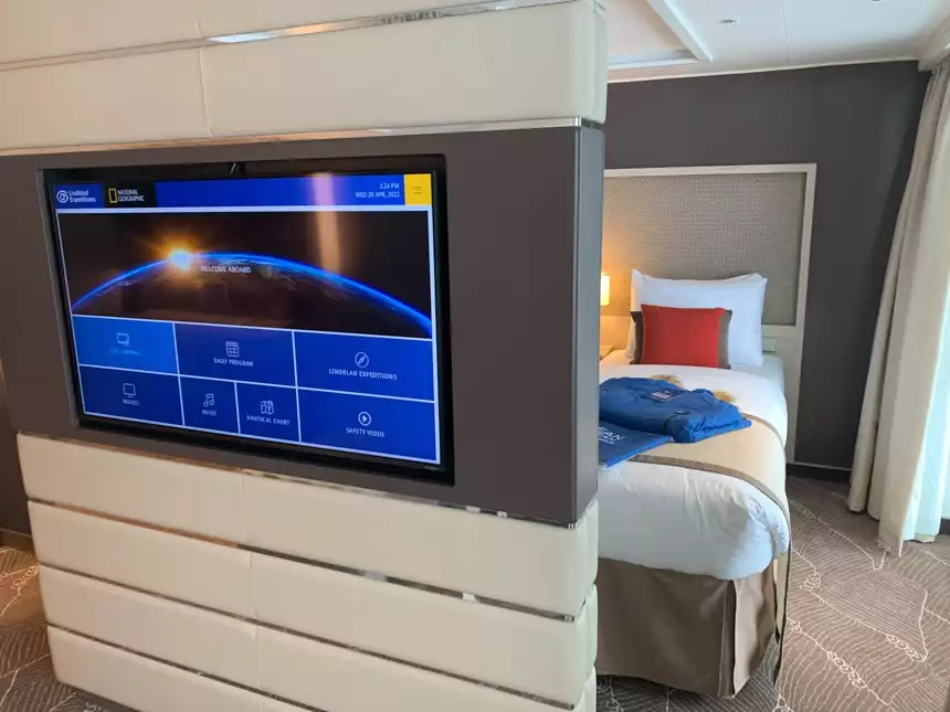 Inside cabin aboard Resolution a free standing white leather wall with a double sided flat screen TV sits before two beds.