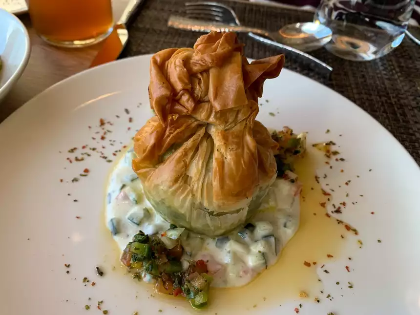 White dinner plate with creamy vegetables surrounded in oil and topped with a filled crunchy wrapped dumpling.