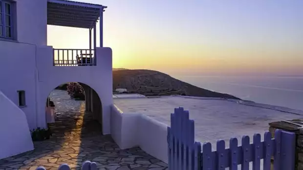 White stucco building with archway and balcony, blue picket fence and cobbled walkway and deck looking out into the ocean.