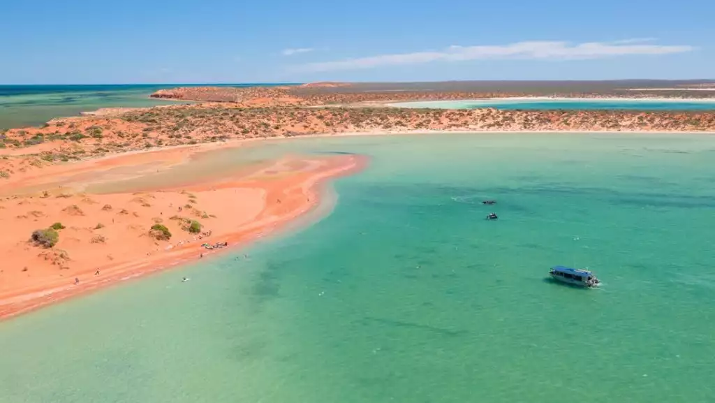 Aerial view of red sand bars with green scrub brush hosting travelers swimming on western Australia cruises.