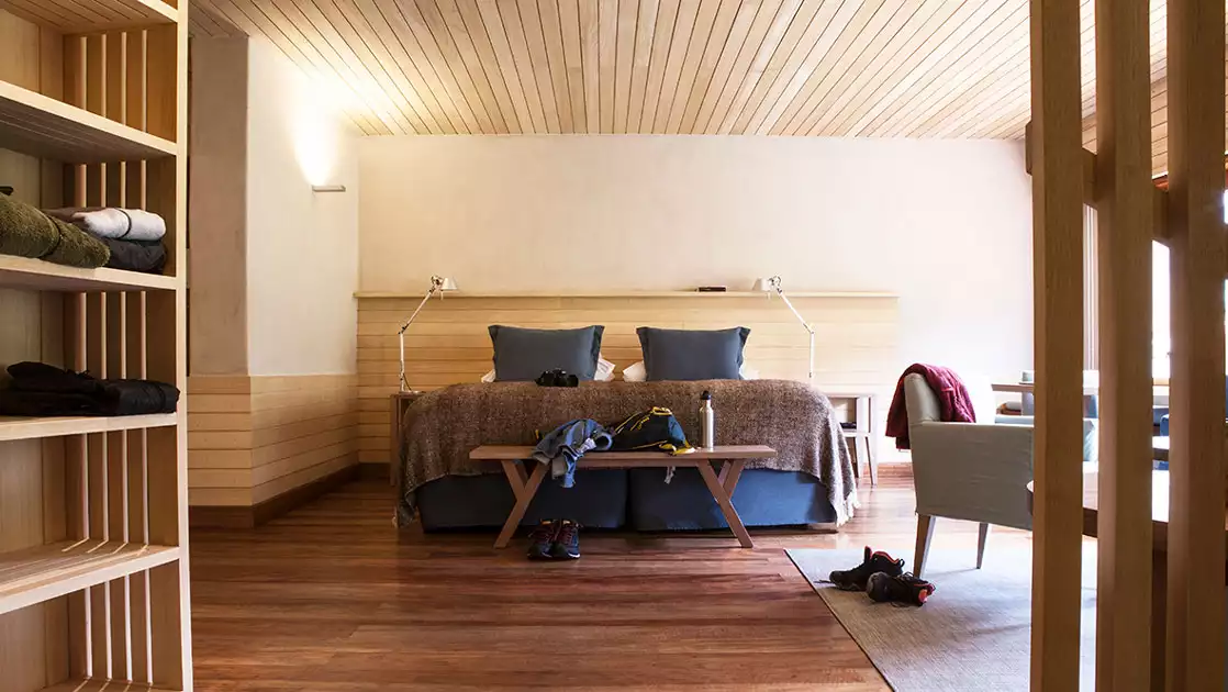 Suite at Explora Sacred Valley Lodge with white stucco walls, wood ceiling & furniture, king bed in rustic decor & lots of light.