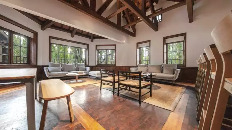 Minimalist common area at Explora Patagonia National Park Lodge with wood floors & seating, windows along each wall & wood beams.