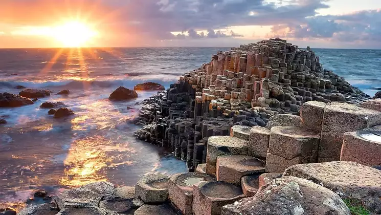 Sunset over the sea by tan circular rock columns on shore, seen on the Treasures of Ireland & The British Archipelagoes trip.