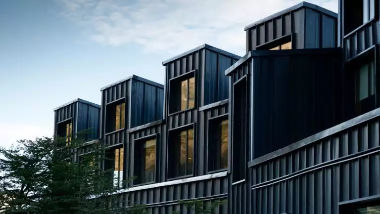 Dark steely exterior of a modern lodge with tall windows sitting beside a tree on the Explora El Chaltén trip.