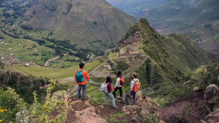 4 Explora Sacred Valley travelers in bright clothes stand atop an outcrop looking down onto Machu Picchu on a hazy day in Peru.