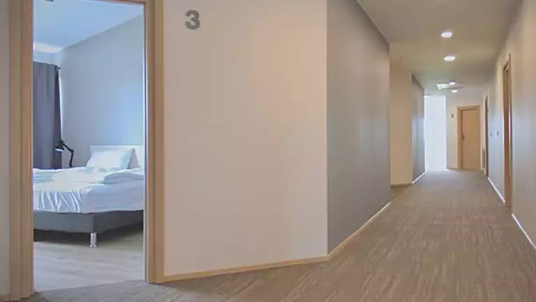 Hallway with door open to guest room #3 at Lilja Guesthouse in southeastern Iceland, with clean beige walls & carpet.