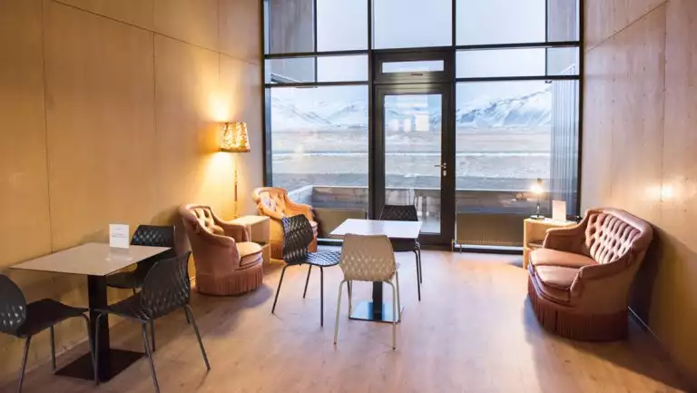 Lounge of Lilja Guesthouse in southeast Iceland with modern, minimalist furniture, tall glass & wood walls & view to snowy peaks.