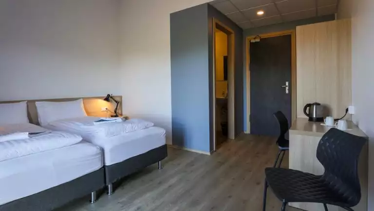 Guest room at Iceland's Lilja Guesthouse looking towards entry door with chair, 2 single beds, desk, tea kettle & wardrobe.