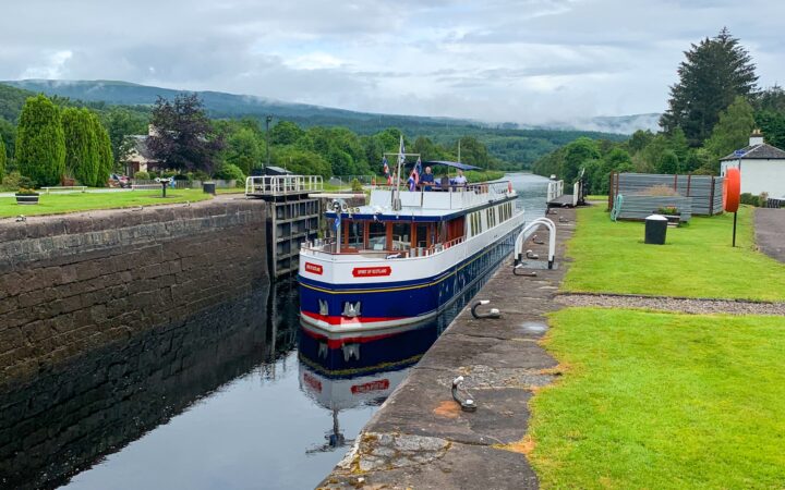The Spirit of Scotland Barge squeezes through the skinny Caledonian canal water way, flanked on either side by tall stone walls.