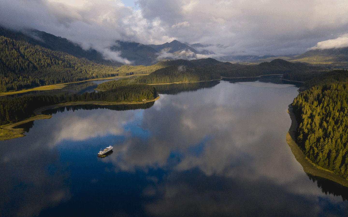 An aerial photo of the small Uncruise cruise ship Wilderness Adventurer seen from above in a still water cove in Alaska