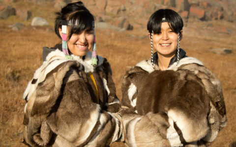 Arctic Inuit boy & girl post for a photo in animal fur coats & beaded headbands while standing among golden tundra.