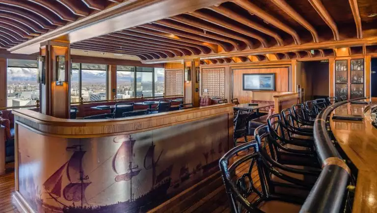Empty bar at Captain Cook Hotel with nautical theme, dark wood beams & furniture, soft lighting & view windows.