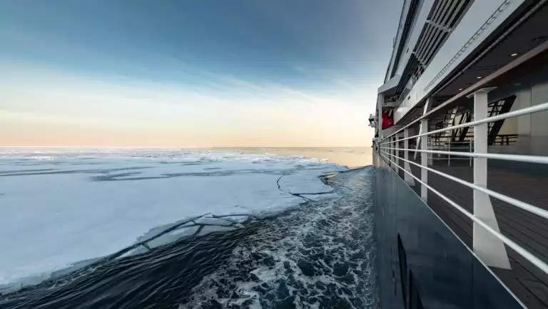 Profile of Le Commandant Charcot small ship with dark blue hull & white upper decks as she cruises to the North Pole by icebergs.