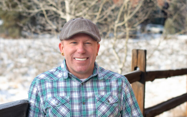 Portrait of Kiel Sprague in a plaid shirt with snowy background and a fence