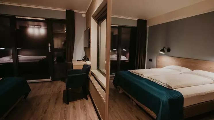 Guest room at Hotel Kria in south Iceland, with wall separating 2 double beds in white & teal, desk, wood floors & big windows.