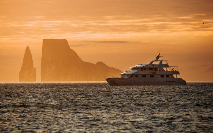 A deep orange sunset over a silhouetted kicker rock and Seaman Journey floats on the horizon line in the Galapagos.