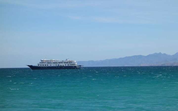 Small ship sailing in the turquoise waters of Baja with faint mountains behind it