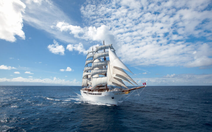 Sea Cloud II: Lindblad 3-masted barque tall ship with white exterior sails in open waters on a partly cloudy day.