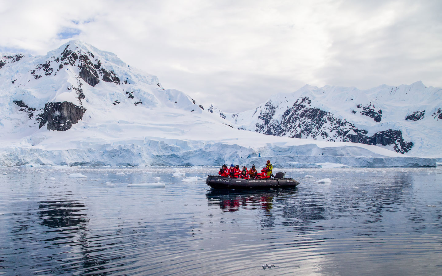 zodiac filled with explorers navigating Antarctica's icy waters in front of snowy white mountains