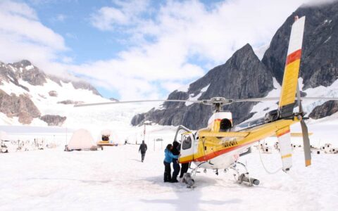 People getting out of a helicopter on top of a glacier next to a dog sledding camp in Alaska on a sunny day