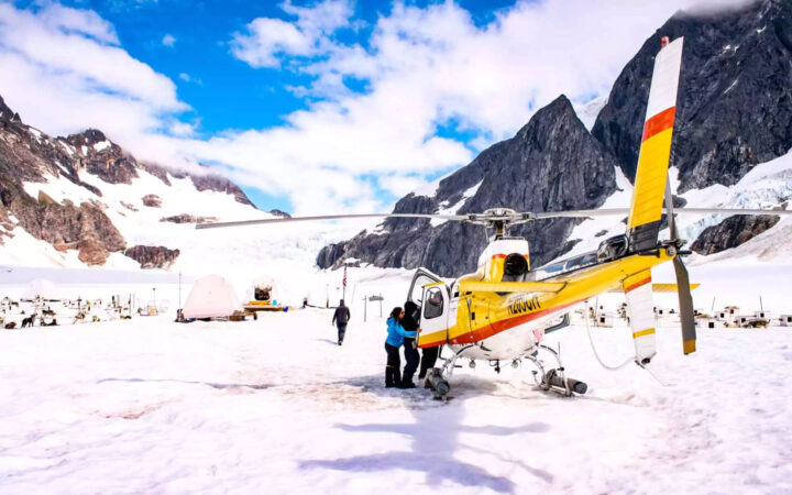 People getting out of a helicopter on top of a glacier next to a dog sledding camp in Alaska on a sunny day