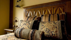 Double bed with paisley throw pillows & bedding & carved wood headboard with bedside table at the Homes at Kenai Riverside Lodge.