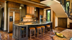 Kitchen of 1 of the Homes at Kenai Riverside Lodge with counter, built-in fridge, wood floor, leather bar stools & pendant lights.