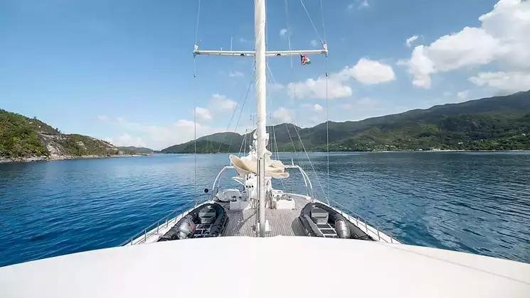 View from upper deck of large white sailboat in Caribbean with sails furled & 2 Zodiac boats sitting on teak deck near bow