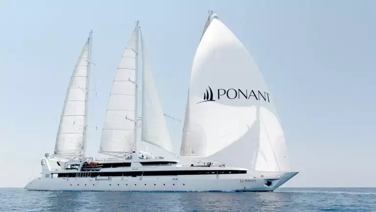 Medium-sized white sailboat Le Ponant with 4 large white sails full of wind sails through calm blue sea in the sun in Greece.