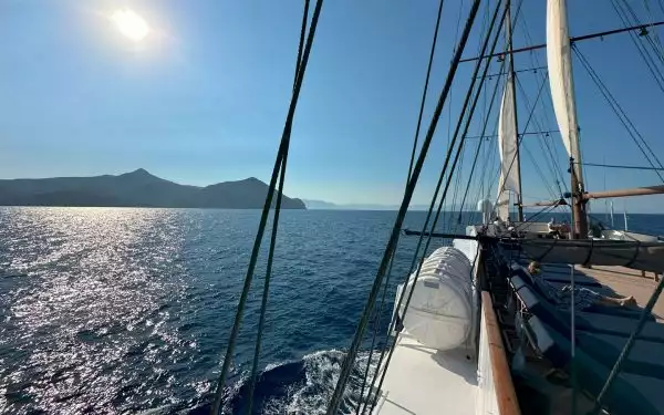 Galileo cruise ship sailing out at sea on a sunny day in Greece with woman on blue padded chaise lounger under rigging & sails.