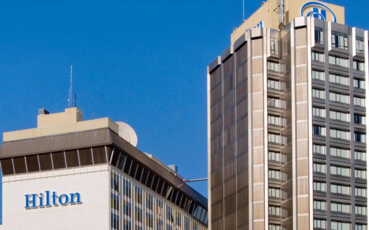 The exterior of the Hilton Downtown Anchorage hotel, blue sunny day, with a tall 600 room building.