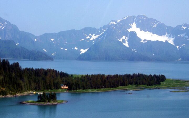 The Kenai Fjords Glacier Lodge is located within the 700,000-acre National Park. A view of the mountains, the Pedersen Glacier, a lake, and the forest where the hotel is nestled.