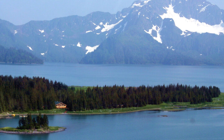 The Kenai Fjords Glacier Lodge is located within the 700,000-acre National Park. A view of the mountains, the Pedersen Glacier, a lake, and the forest where the hotel is nestled.