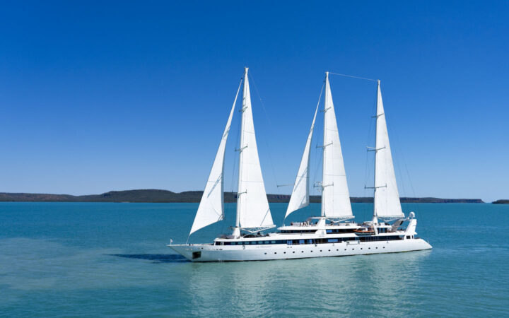 Exterior of Le Ponant white small sailing ship with 3 masts & 5 sails cruising in calm turquoise water on a sunny day.