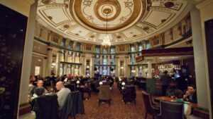 Chandelier hanging in center of dining room with diners seated in leather-backed chairs in Fort Garry Hotel in Winnipeg