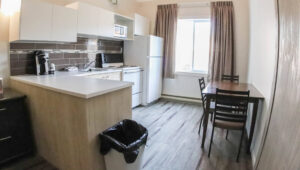 Kitchen with electric stove, sink, counter, refrigerator, cabinets, coffeemaker, table and 3 chairs at the Polar Inn in Churchill, Canada.