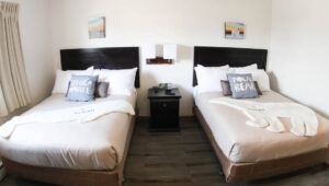 Two double beds with tan bedspreads topped by a fleece cutout of a polar bear or beluga whale, side table in between and two small polar bear paintings above at the Polar Inn in Churchill, Canada.