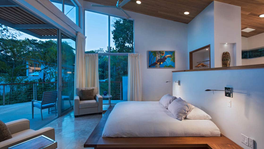 Tropical bird painting adorning wall near bed, steps away from expansive patio and views of lush jungle at Chaa Creek Jungle Lodge in Belize