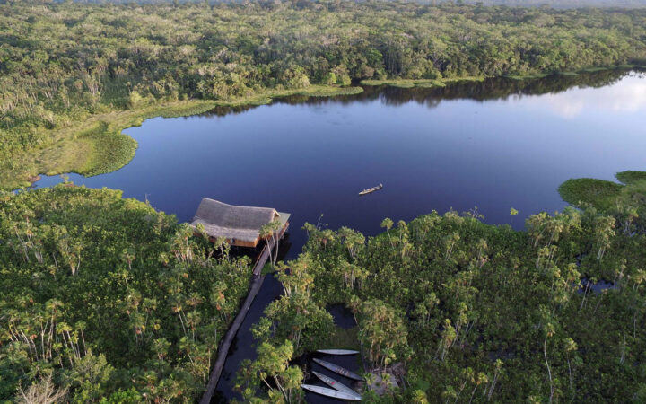 An aerial view of the Sacha Jungle Lodge, a sustainable hotel nestled in the Ecuadorian Amazon on the edge of a lake with 26 private thatched-roof cabins.
