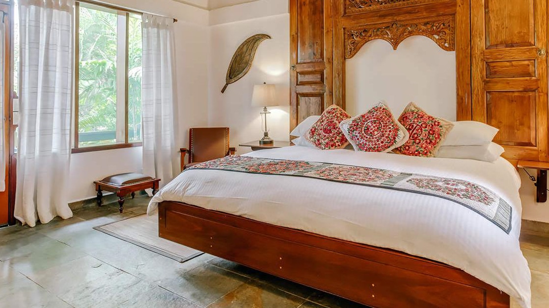 King bed with local decorative pillows framed by a large wood headboard in a cottage bedroom at the Lodge at Chaa Creek in Belize.
