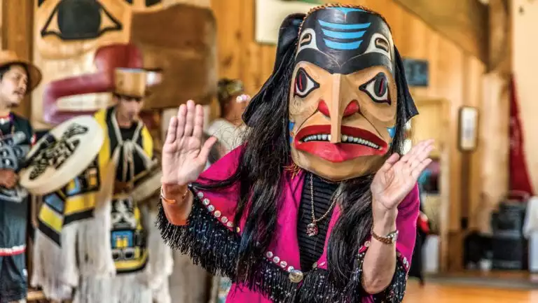 Woman in pink robe with black fringe & native carved wooden mask dances for a cultural presentation on the Remarkable Journey.