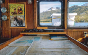 Bridge on Ursus ship in Alaska with nautical maps, binoculars, view windows & bear photos hung on wood-paneled walls.