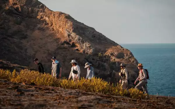 A small group of hikers seen on a brushy brown Galapagos cliffside hiking above the ocean