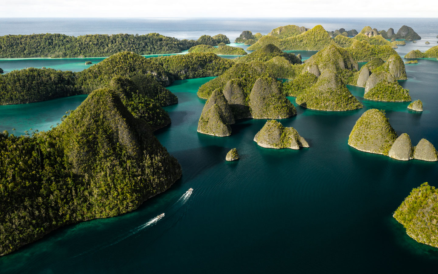 Aerial view of karst gum drop islands in turquoise sea with 2 small Zodiac boats cruising under bright skies in Indonesia.