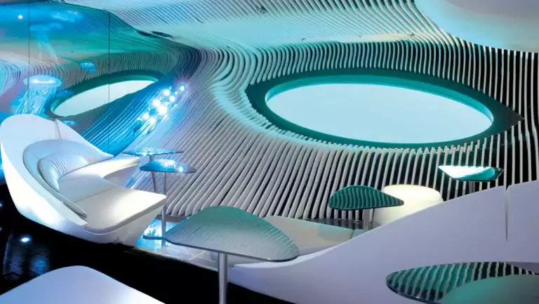 Blue eye lounge on Le Laperouse ship with modern, aquatic-themed white leather couches, mirrors, tables & large underwater window.