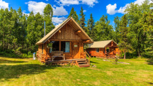 Exterior of guest cabins at Winterlake Lodge with log cabin construction, front porch with a bench & grass & forest surrounding.